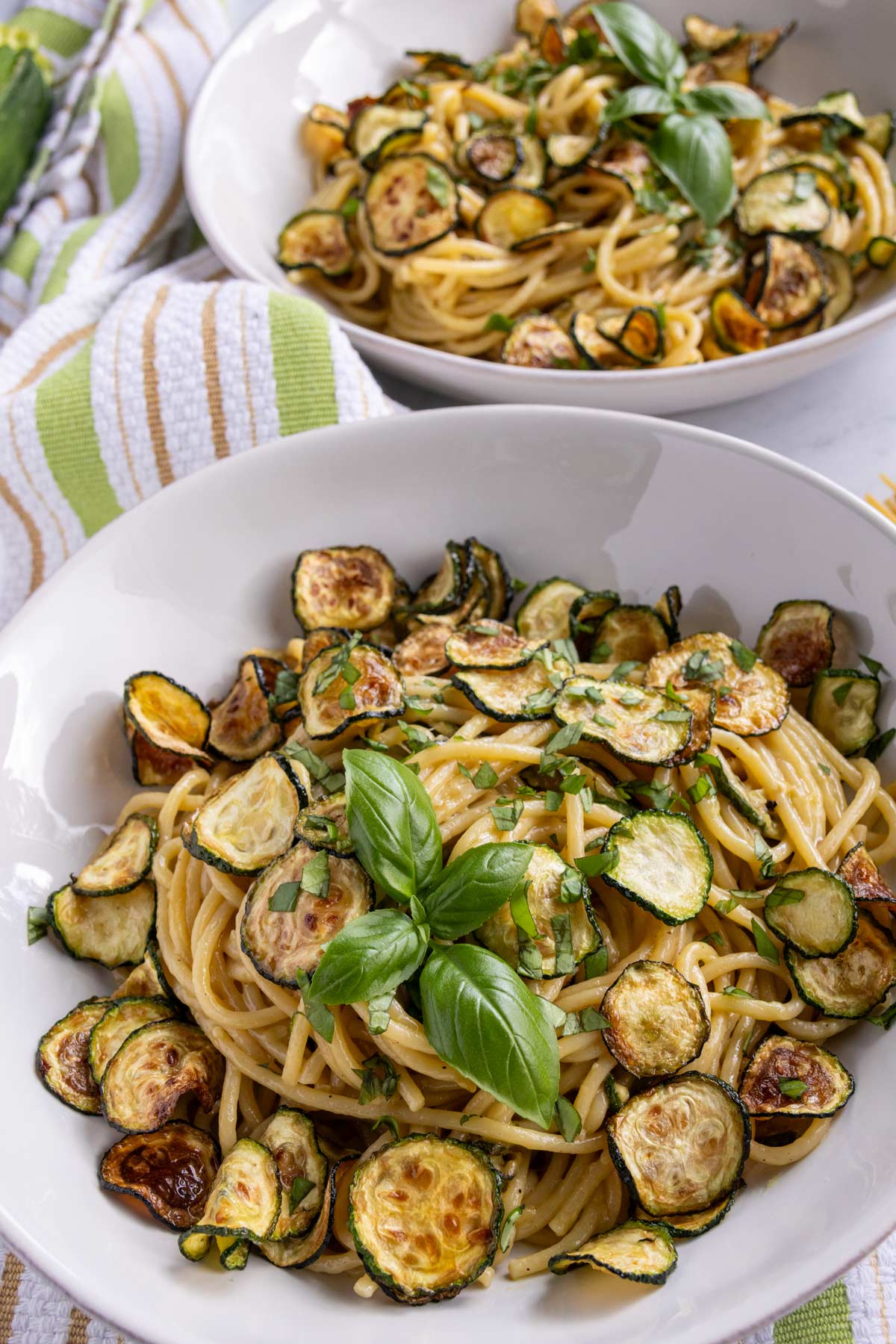 Two wide bowls of spaghetti alla nerano topped with fried zucchini coins and basil.