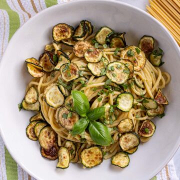 Spaghetti alla nerano topped with fried zucchini coins and a sprig of fresh basil.