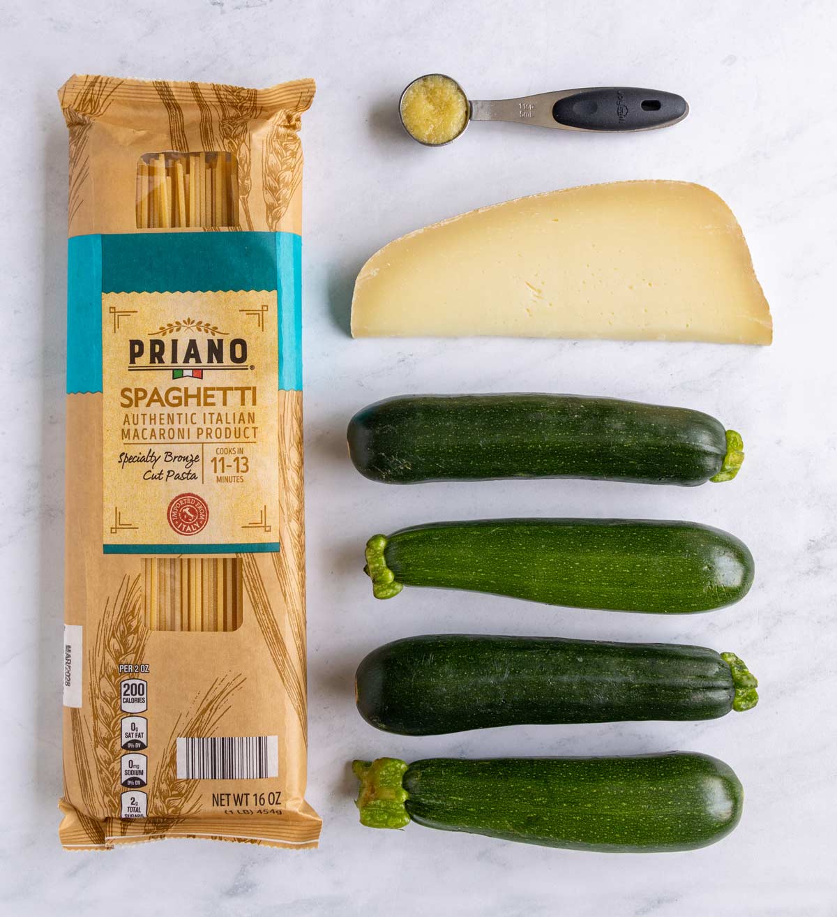 Ingredients for spaghetti alla nerano on a white marble background.