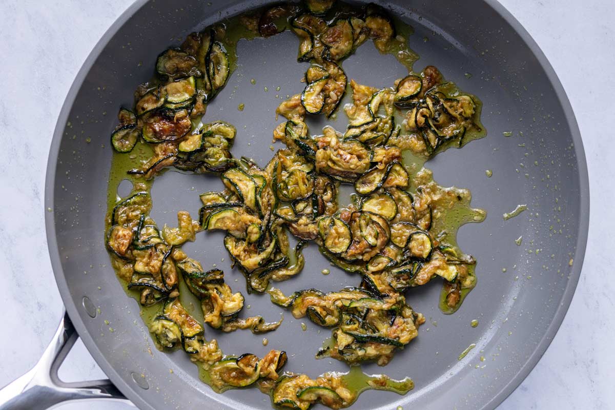 Fried zucchini coins lightly mashed up in a skillet with olive oil and garlic.