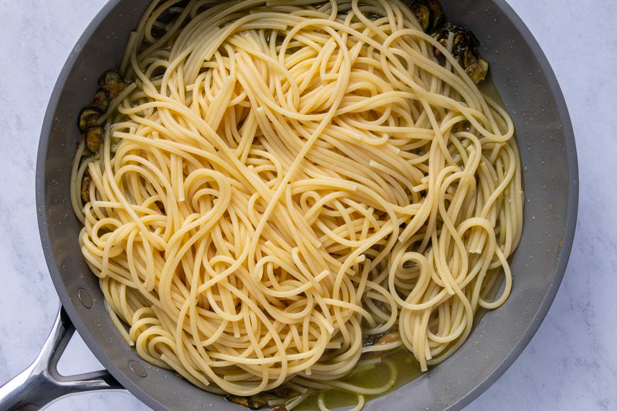 Cooked spaghetti added to a skillet along with some of the starchy pasta water.