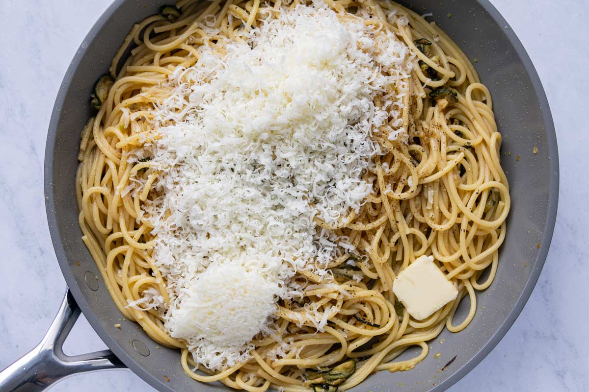 Freshly grated cheese, black pepper, and a small pat of butter added to a skillet of spaghetti.