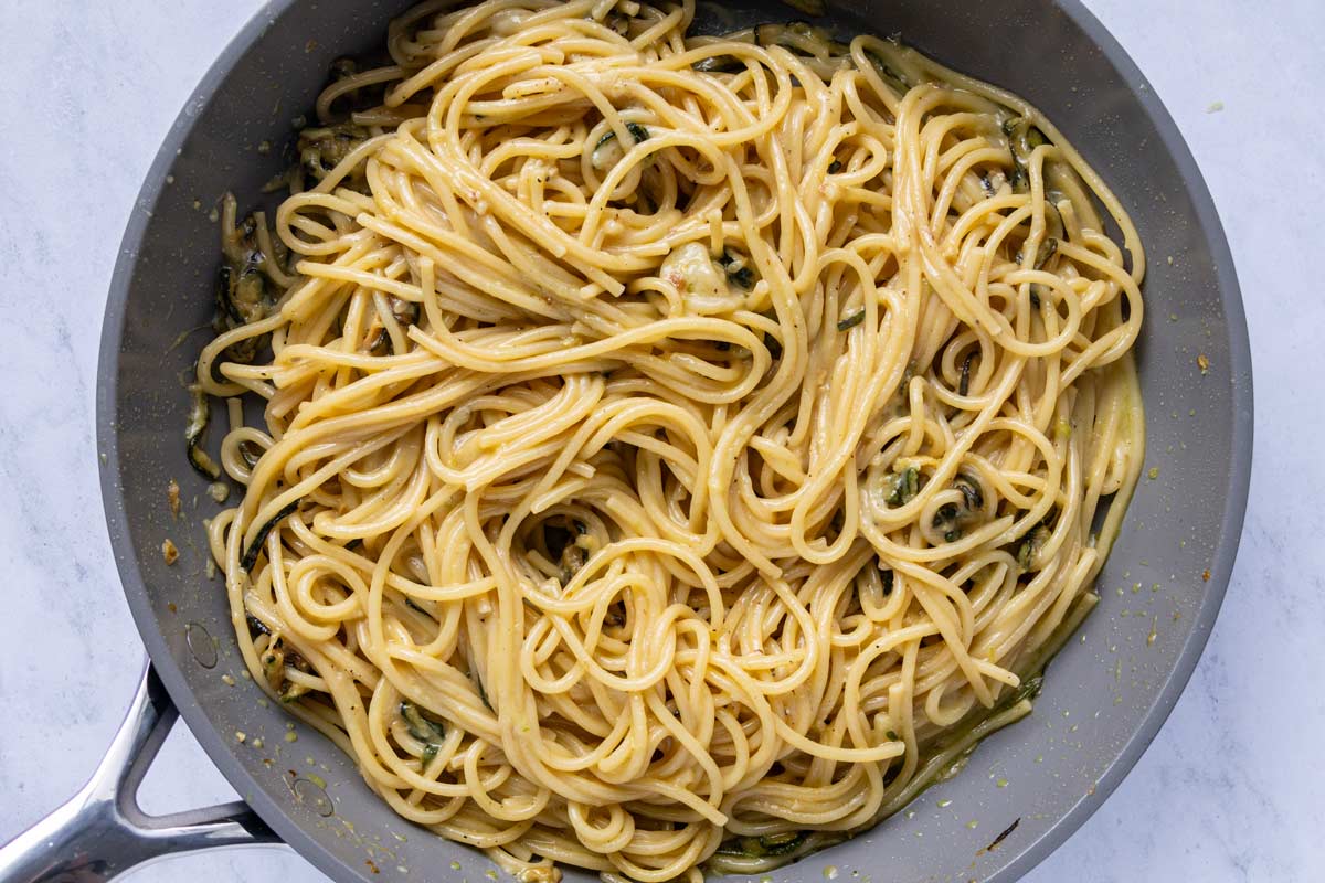 A silky and cheesy mixture of spaghetti and fried zucchini in a nonstick skillet.