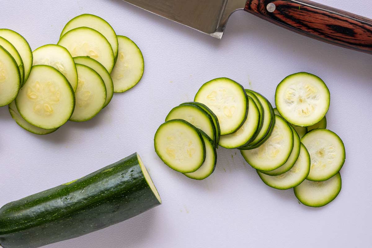 Slicing zucchini into thin coins on a cutting board.