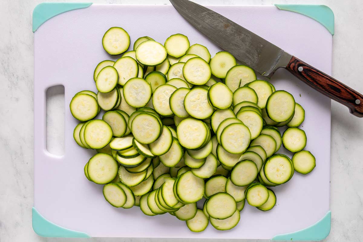 Thinly sliced zucchini alongside a knife on a cutting board.