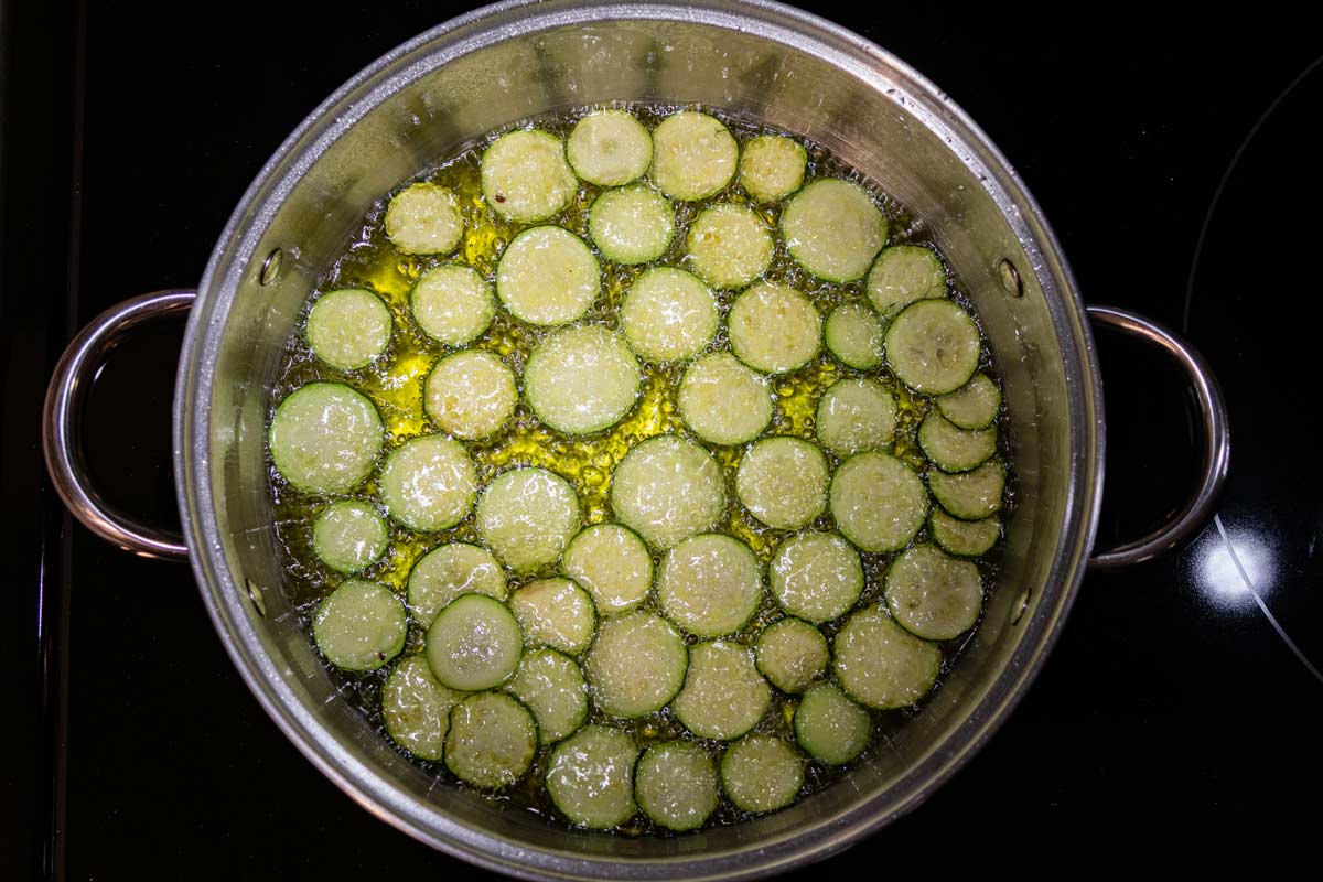 Slices of zucchini added to a pot of hot oil on the stovetop.