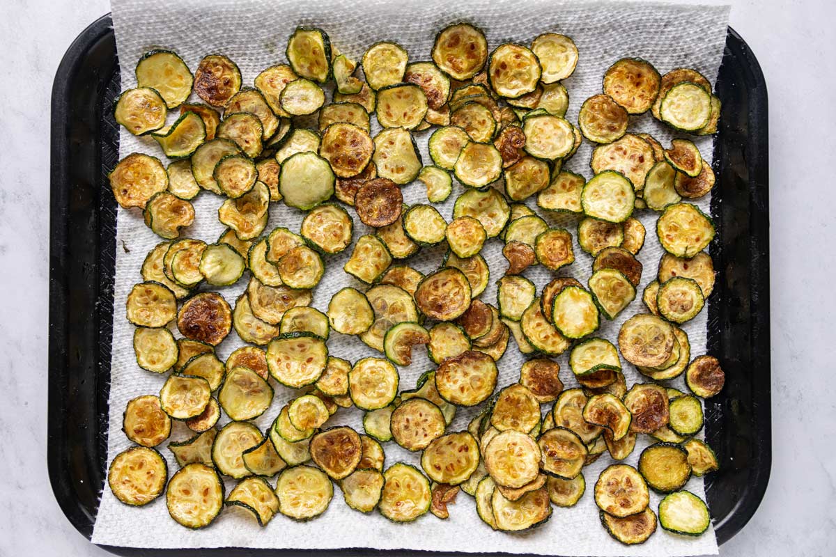 Thinly sliced, fried zucchini coins on a paper towel lined tray.