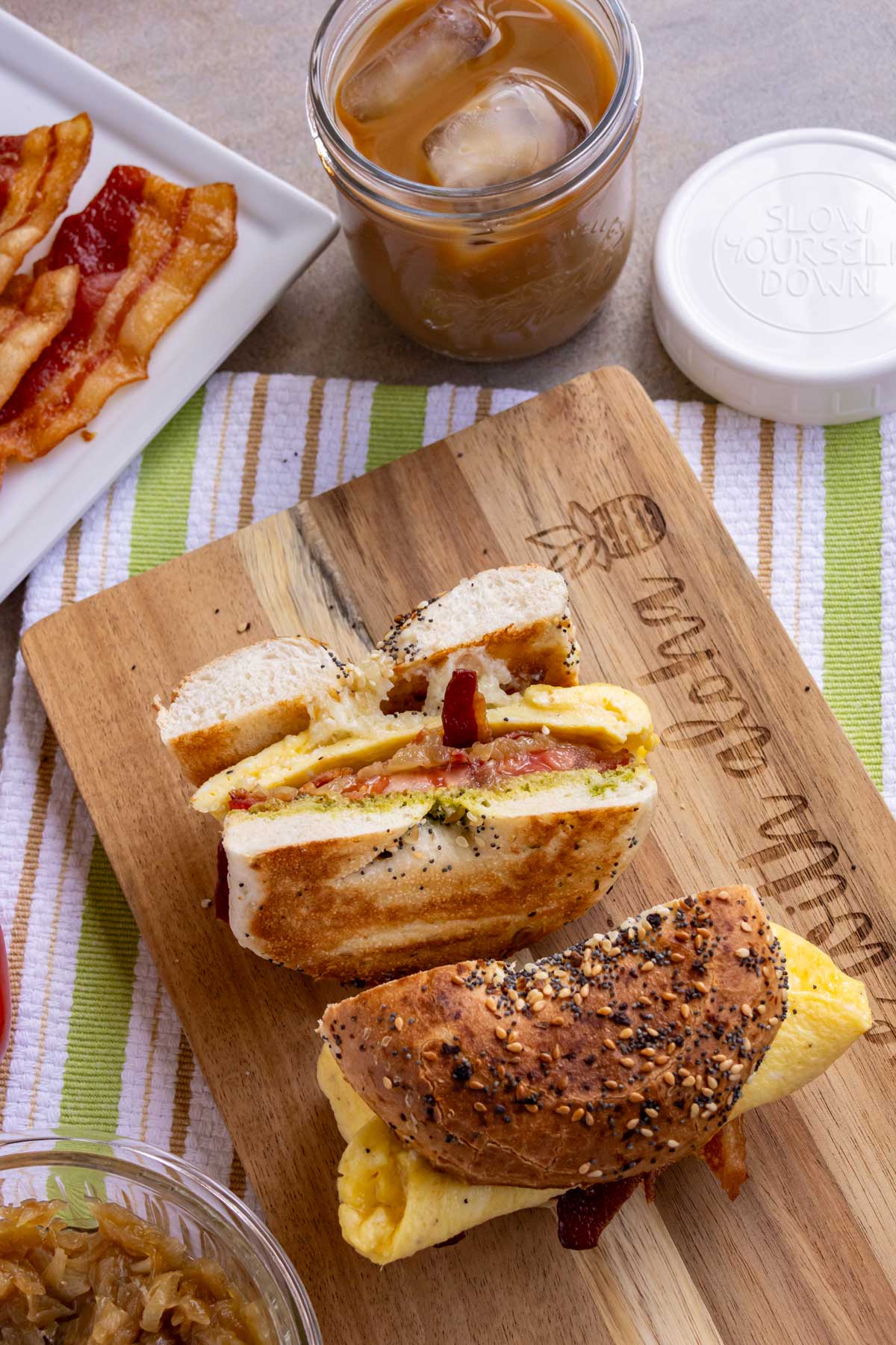 A breakfast sandwich on an everything bagel filled with egg, cheese, pesto, tomato, caramelized onions, and bacon.