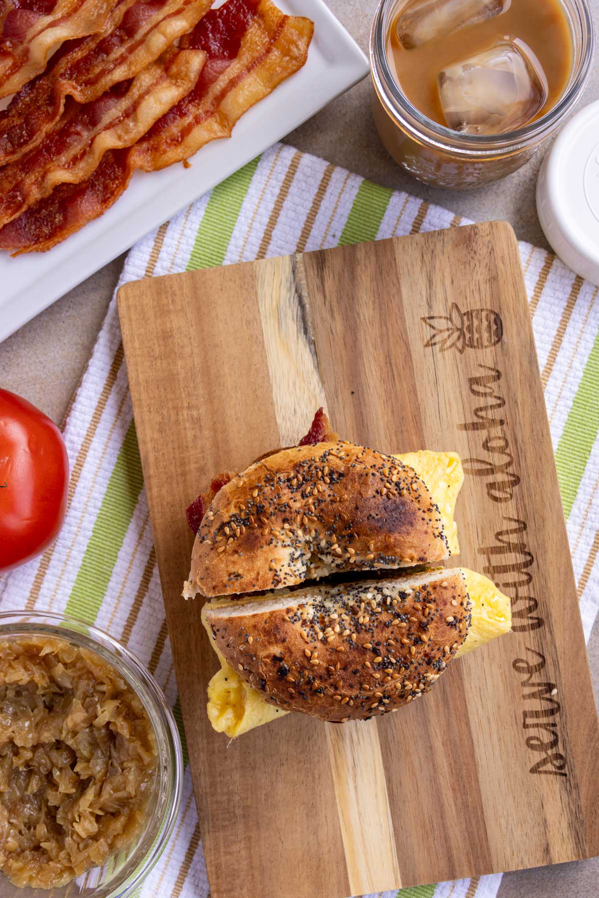 A breakfast sandwich made on an everything bagel on a board that says Serve with Aloha.