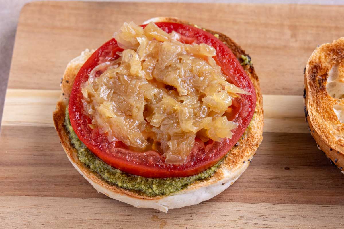 Pesto, a slice of tomato, and caramelized onions on the bottom of a toasted bagel.